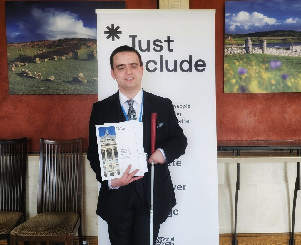 Andrew Hamilton holding just include leaflets on front of just Include banner