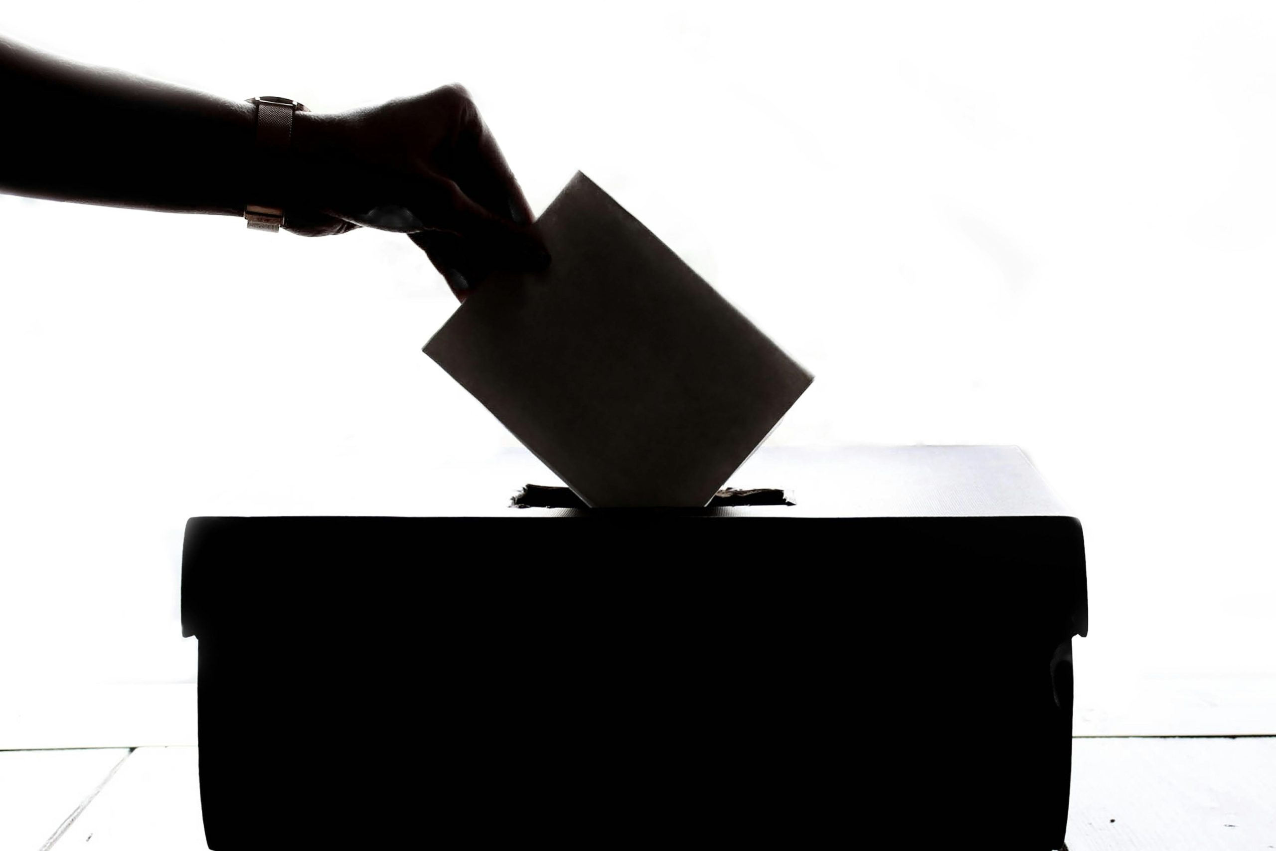 sillohette of hand putting a voting slip in a ballot box